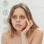 woman looking at dark circles under eye in mirror